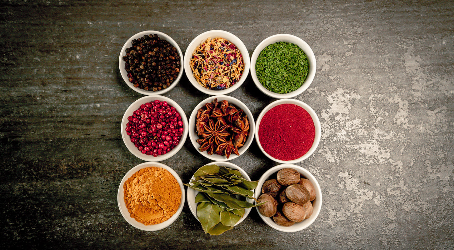 A collection of colorful spices arranged in small bowls on a wooden table, showcasing a variety of textures and hues.